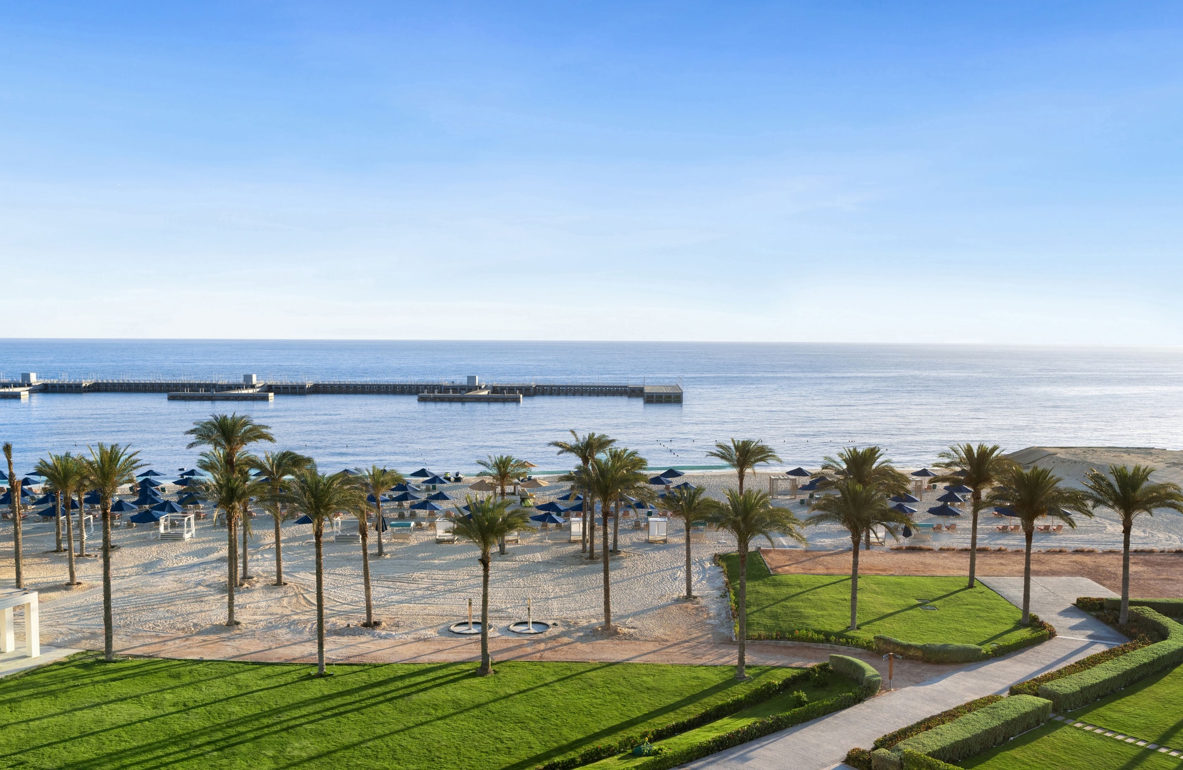 Песчаный пляж Rixos Premium Alamein с пальмами, зонтиками и пирсом